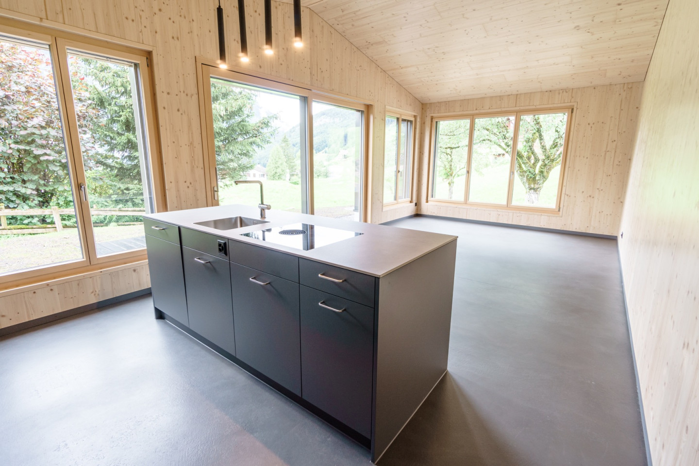 Offene Küche mit dunkler Kochinsel und grossen Fenstern zu Garten und Bergen