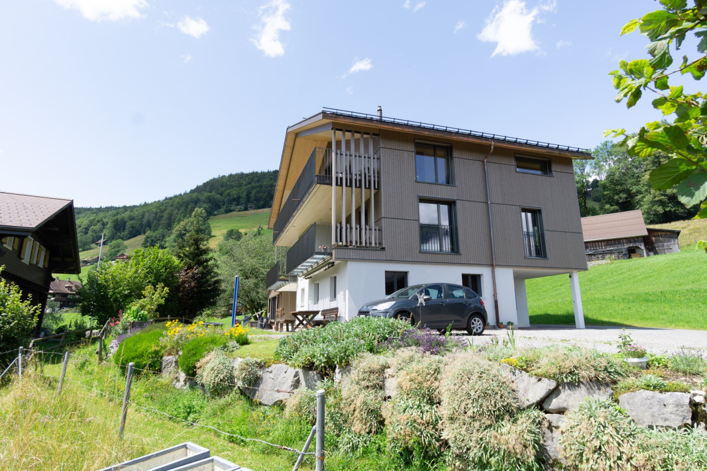 Wohnhaus mit auskragendem Balkon auf Stützen, umgeben von Wiesen und Wald